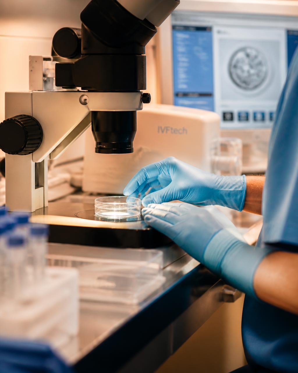Embryologist in a fertility laboratory preparing a petri dish for evaluation under a microscope